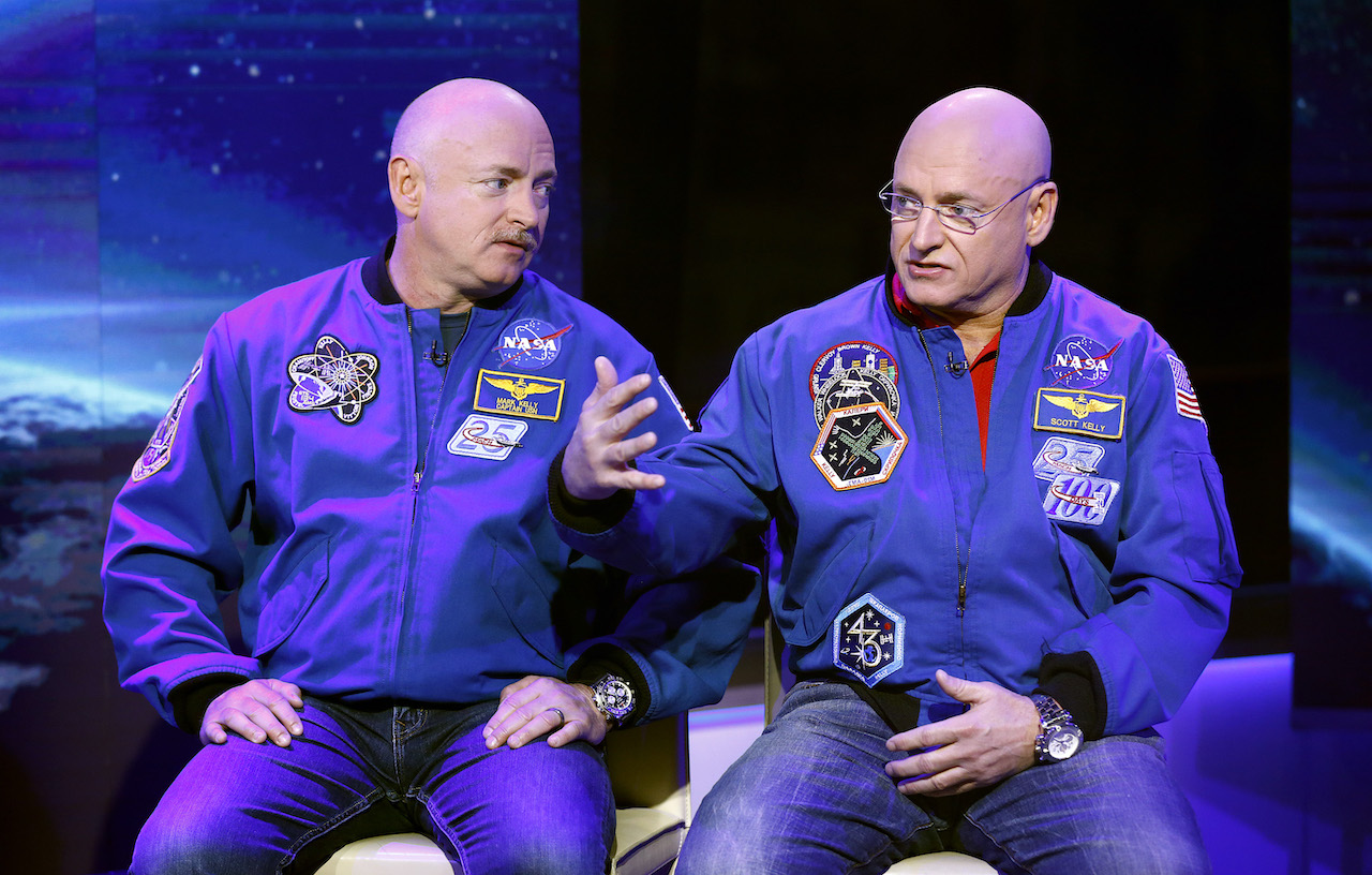 Scott și Mark Kelly stau unul lângă altul purtând o jachetă albastră NASA și blugi